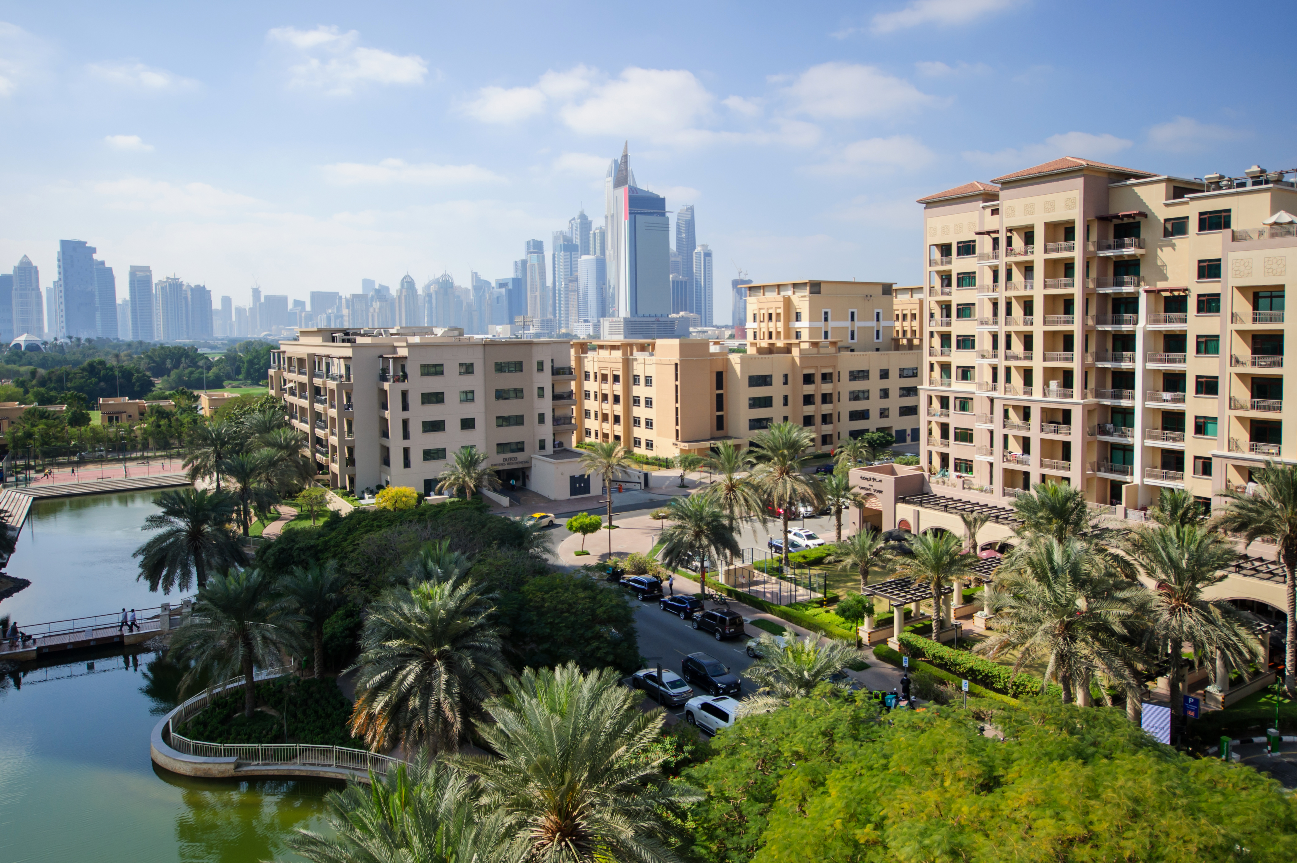 Greens Community in Dubai with mid-rise residential buildings, landscaped gardens, and tranquil water features under a clear blue sky.