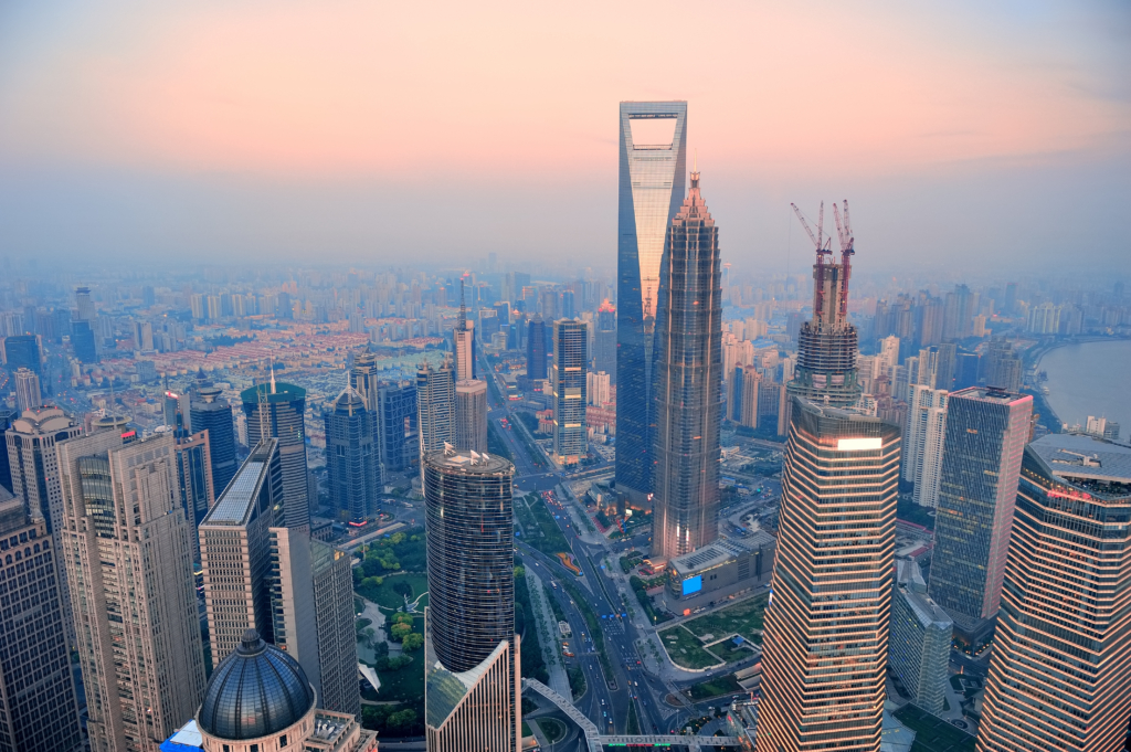 Aerial view of Shanghai skyline at sunset featuring the Oriental Pearl Tower, skyscrapers, and Huangpu River in golden light.